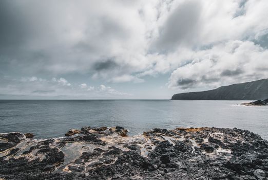 Stunning view of a rocky shoreline under cloudy skies with distant cliffs, capturing the beauty of the sea.