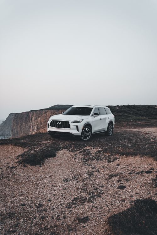 Free A white SUV parked on a rocky cliff overlooking the ocean at sunset, exuding adventure and exploration. Stock Photo