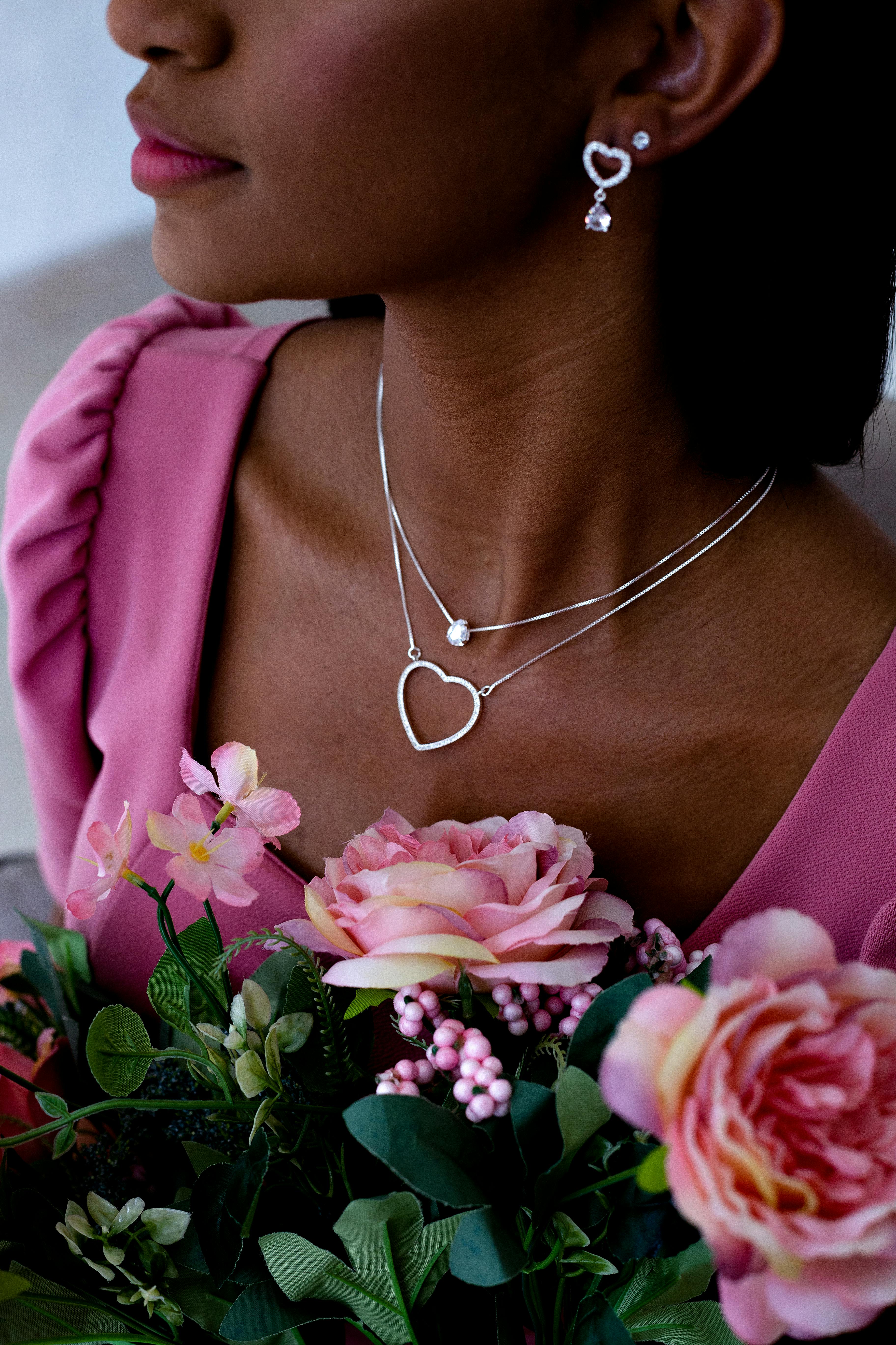 Portrait of a woman with heart-shaped jewelry and pink flowers, capturing elegance and femininity.