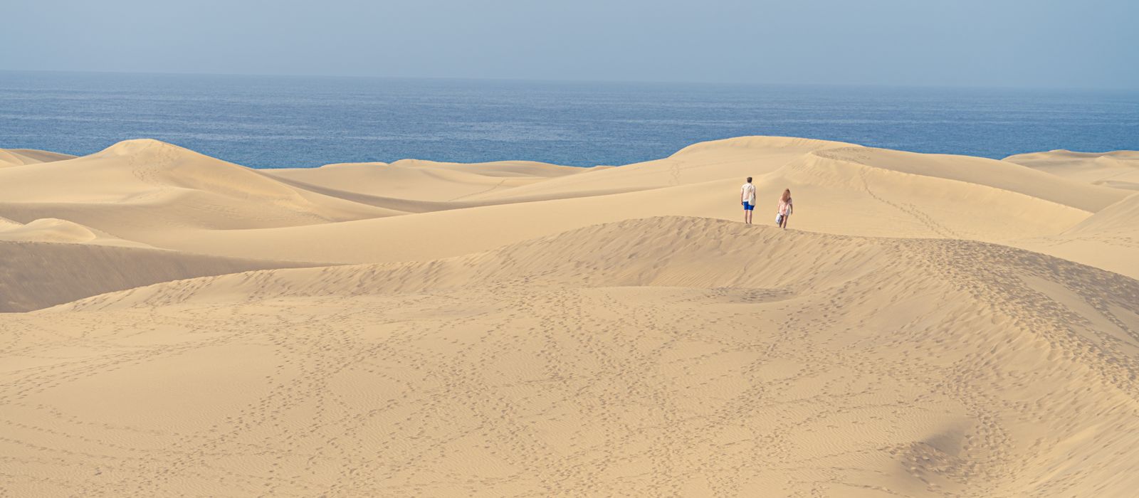 Peaceful dunes of Maspalomas in Spain with ocean views and two people exploring.