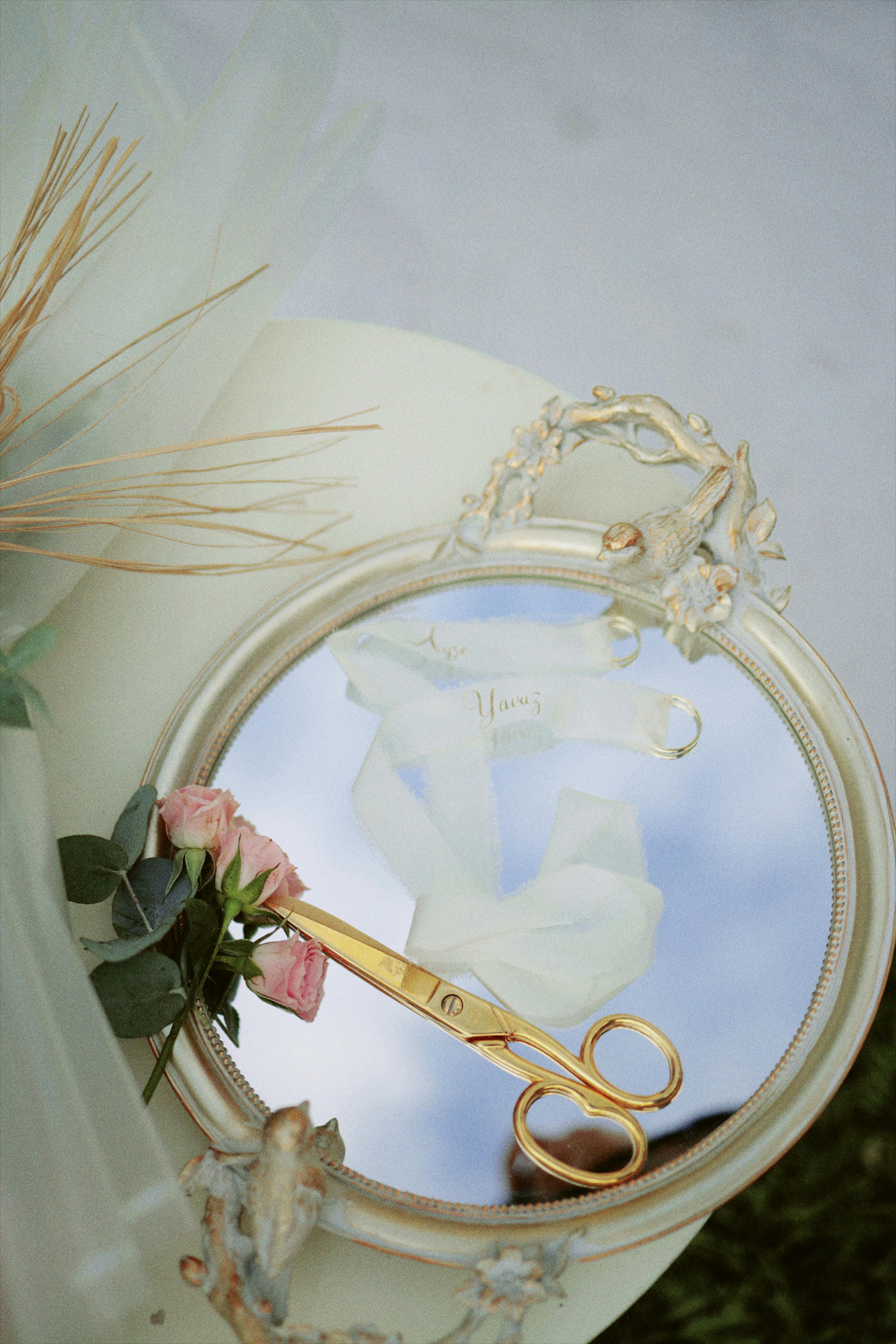 Stylish wedding decor with gold scissors on ornate mirror reflecting sky.