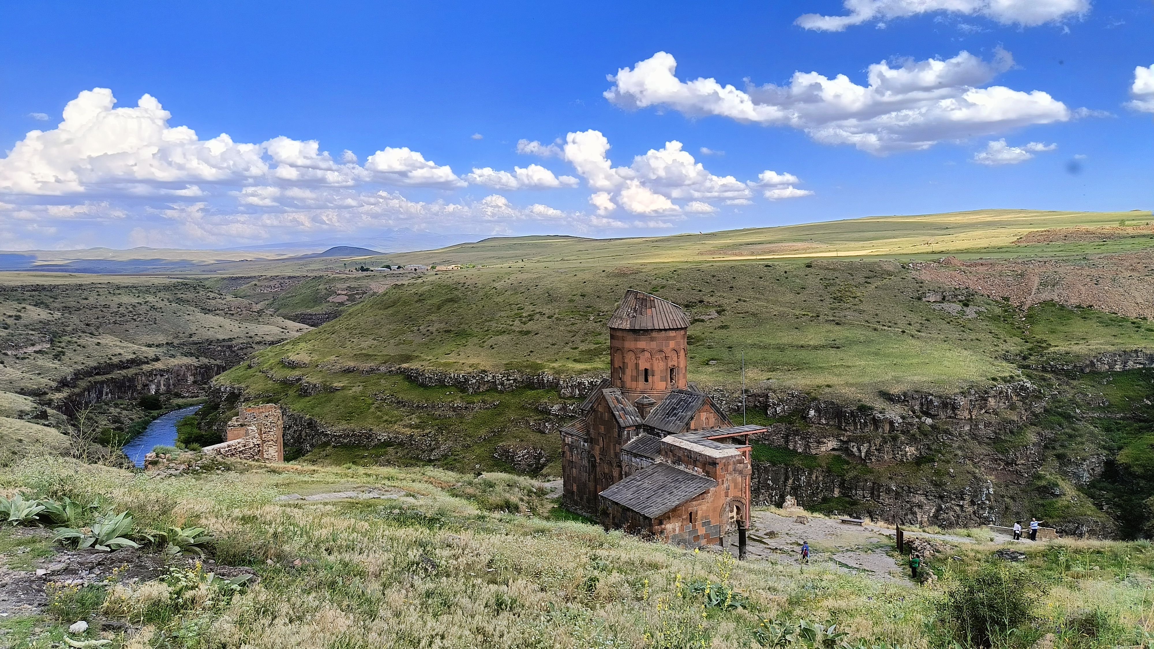 A picturesque view of an ancient church amidst rolling hills and a bright blue sky.