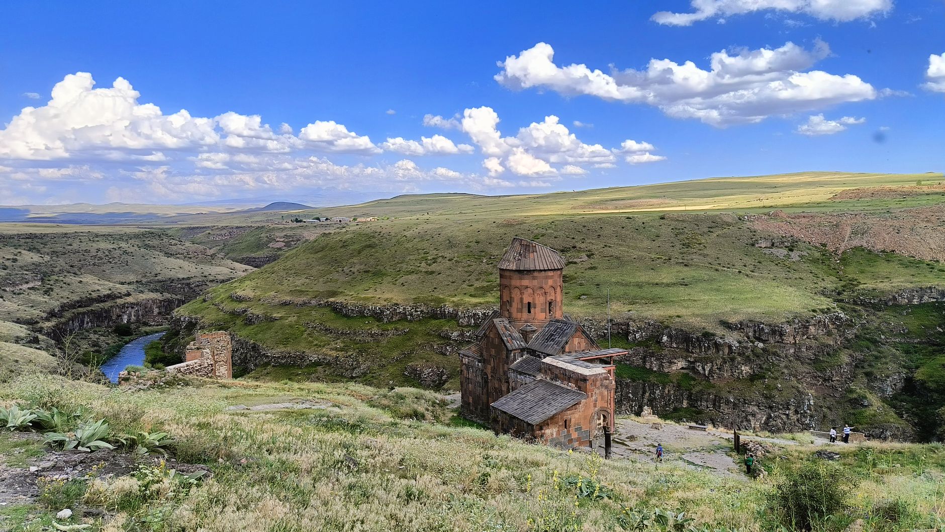 A picturesque view of an ancient church amidst rolling hills and a bright blue sky.
