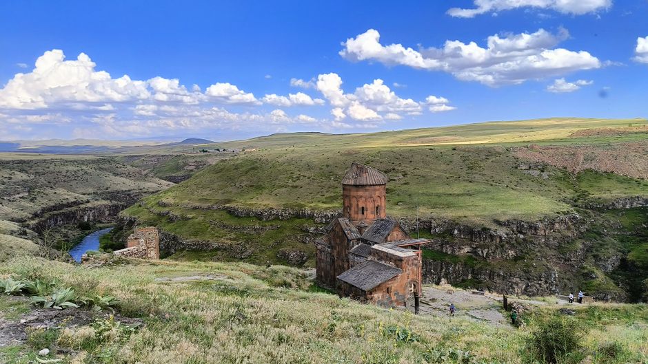 A picturesque view of an ancient church amidst rolling hills and a bright blue sky.