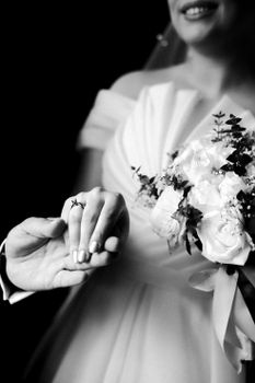 A classic black and white photo capturing a bride holding flowers and showing off wedding rings.