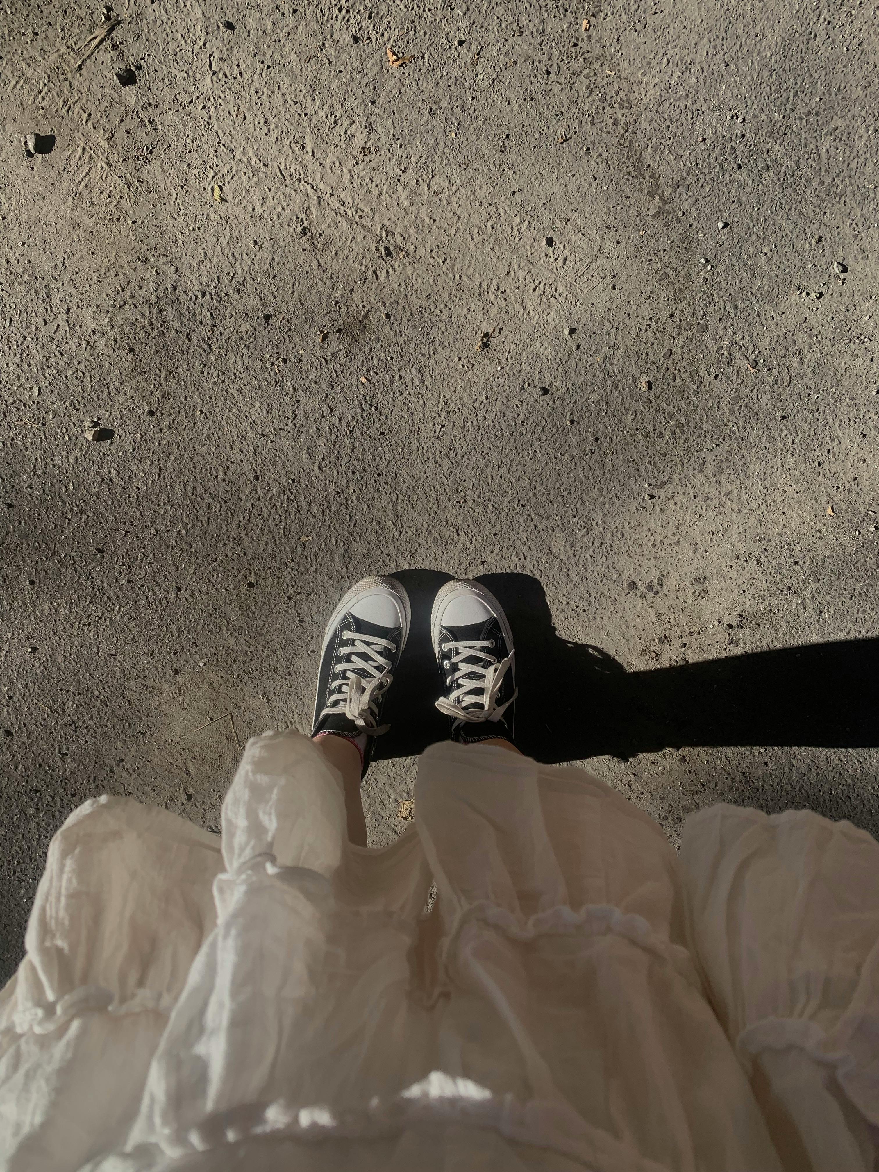 Feet in Converse sneakers casting shadow on sunlit pavement.