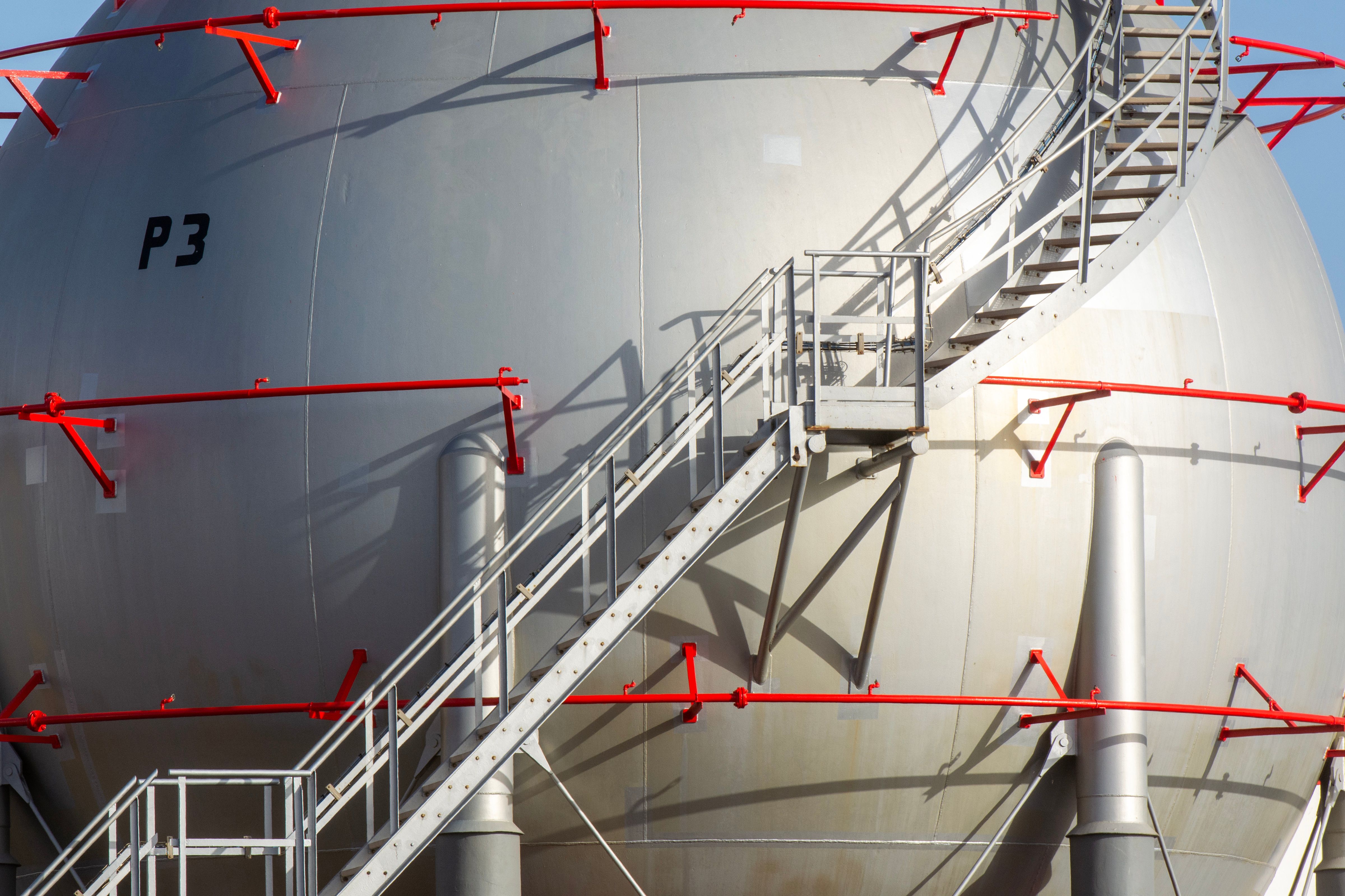 Large industrial storage tank with metal staircase and red railings, symbolizing progress.