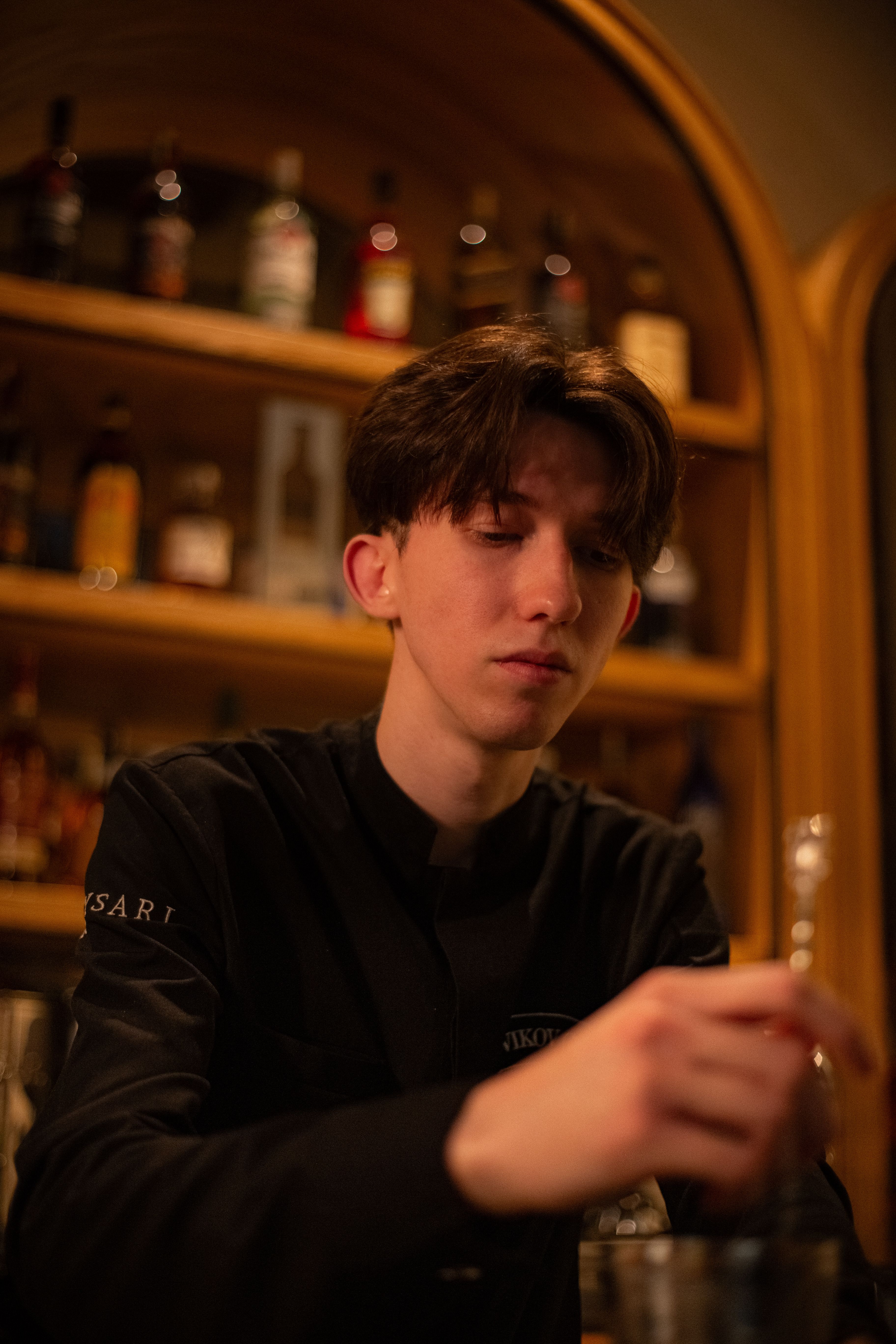 A young bartender preparing drinks in a cozy, dimly lit bar environment.
