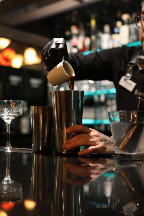 Free Bartender skillfully pouring ingredients to create a refined cocktail in a stylish bar setting. Stock Photo
