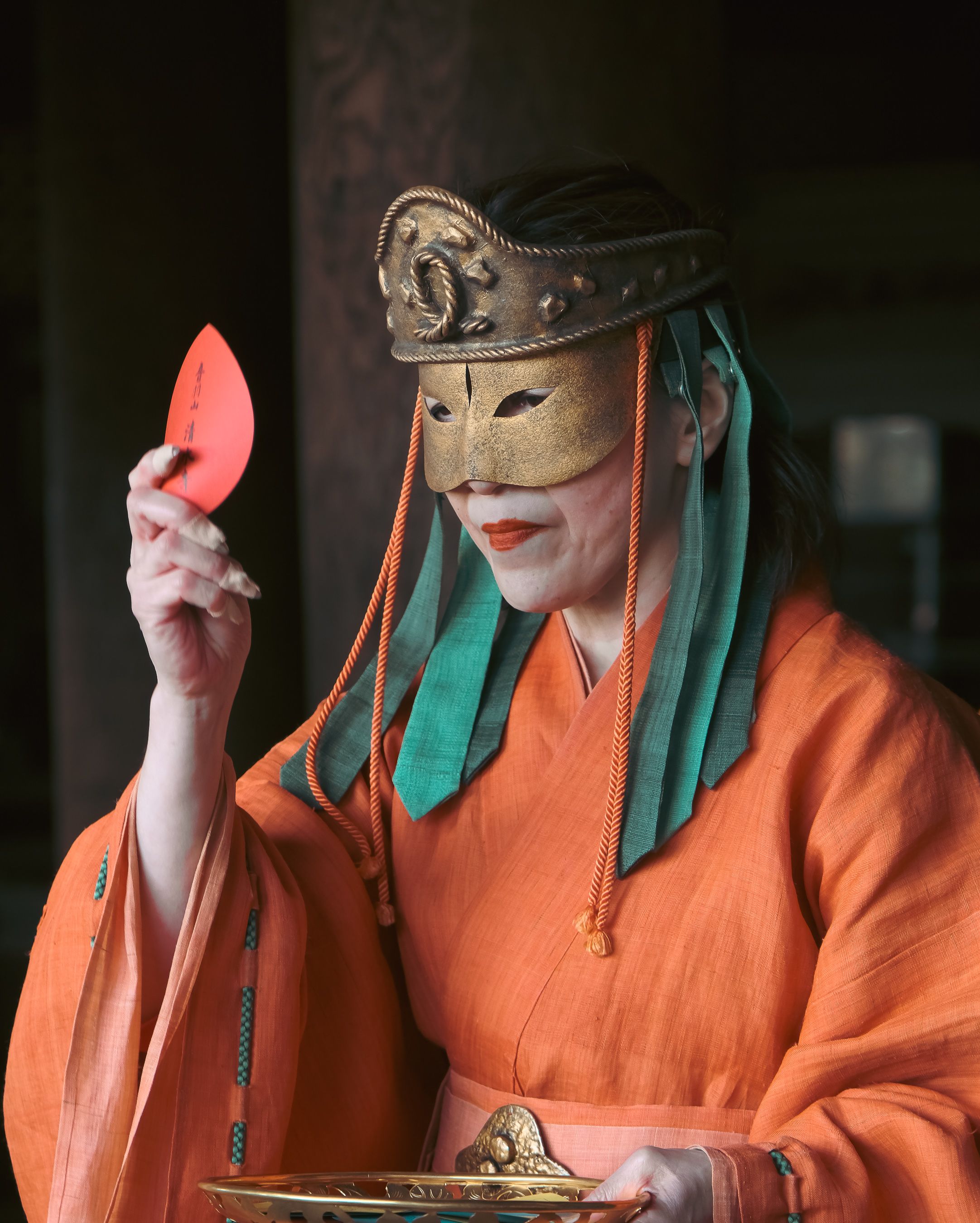 A person in traditional Japanese attire wearing a mask, holding a red card.