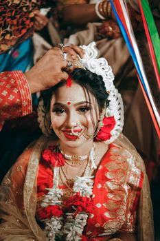 A radiant Indian bride in traditional attire during a wedding ceremony, adorned with jewelry and floral garlands.