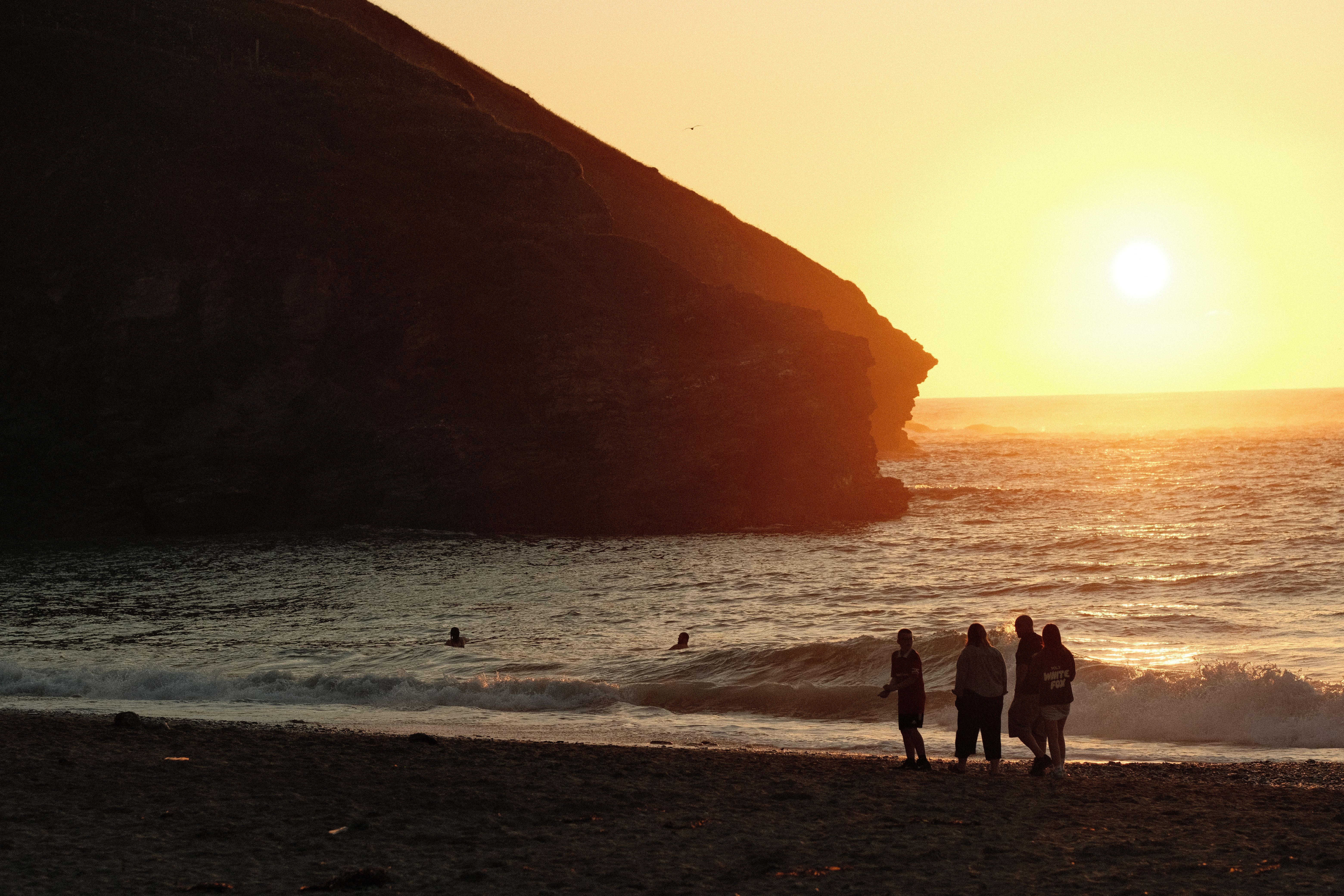 A group of people enjoying a sunset view on a beach with cliffs in the background.