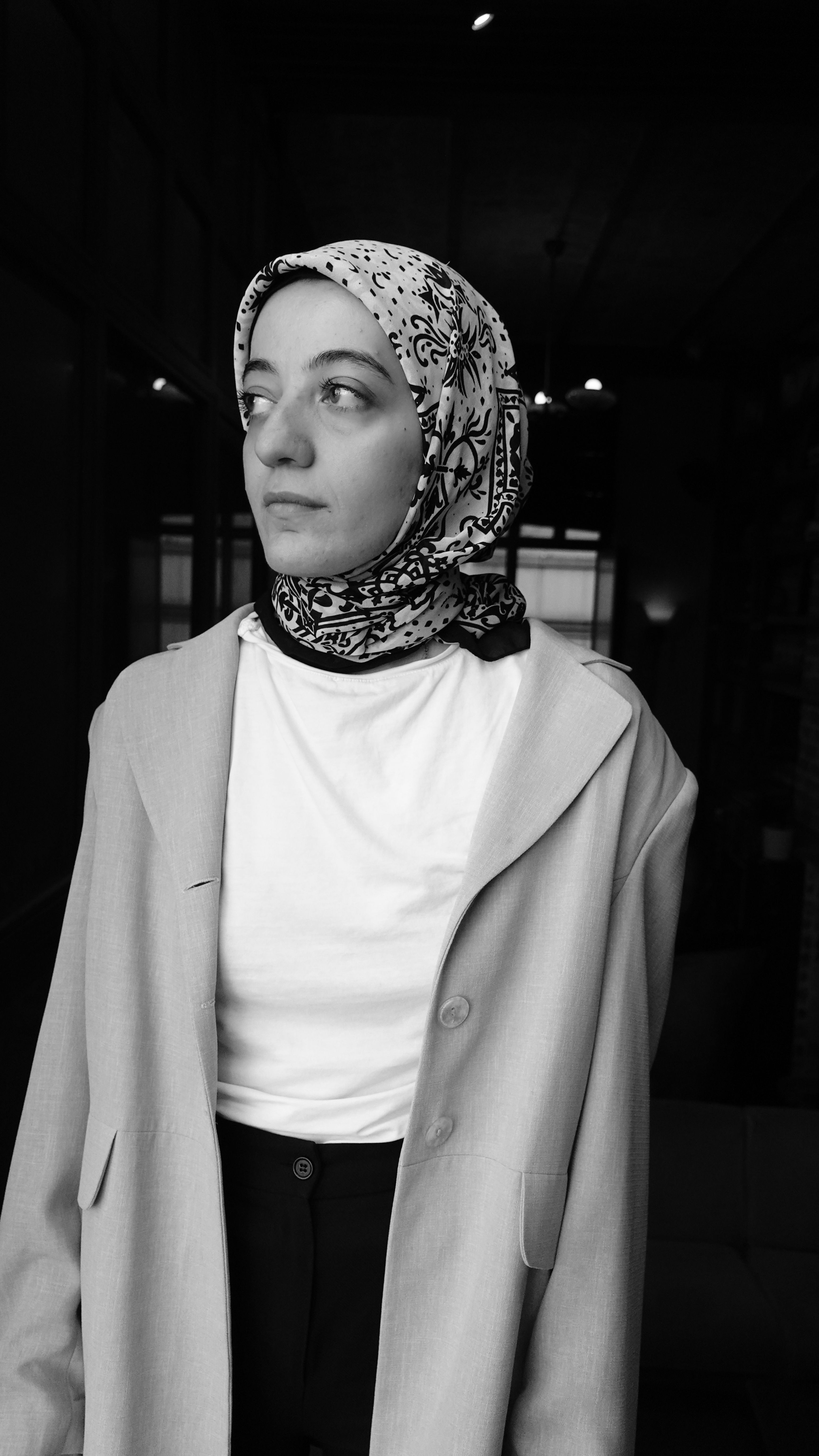 Black and white portrait of a woman with a headscarf indoors, conveying elegance and fashion.