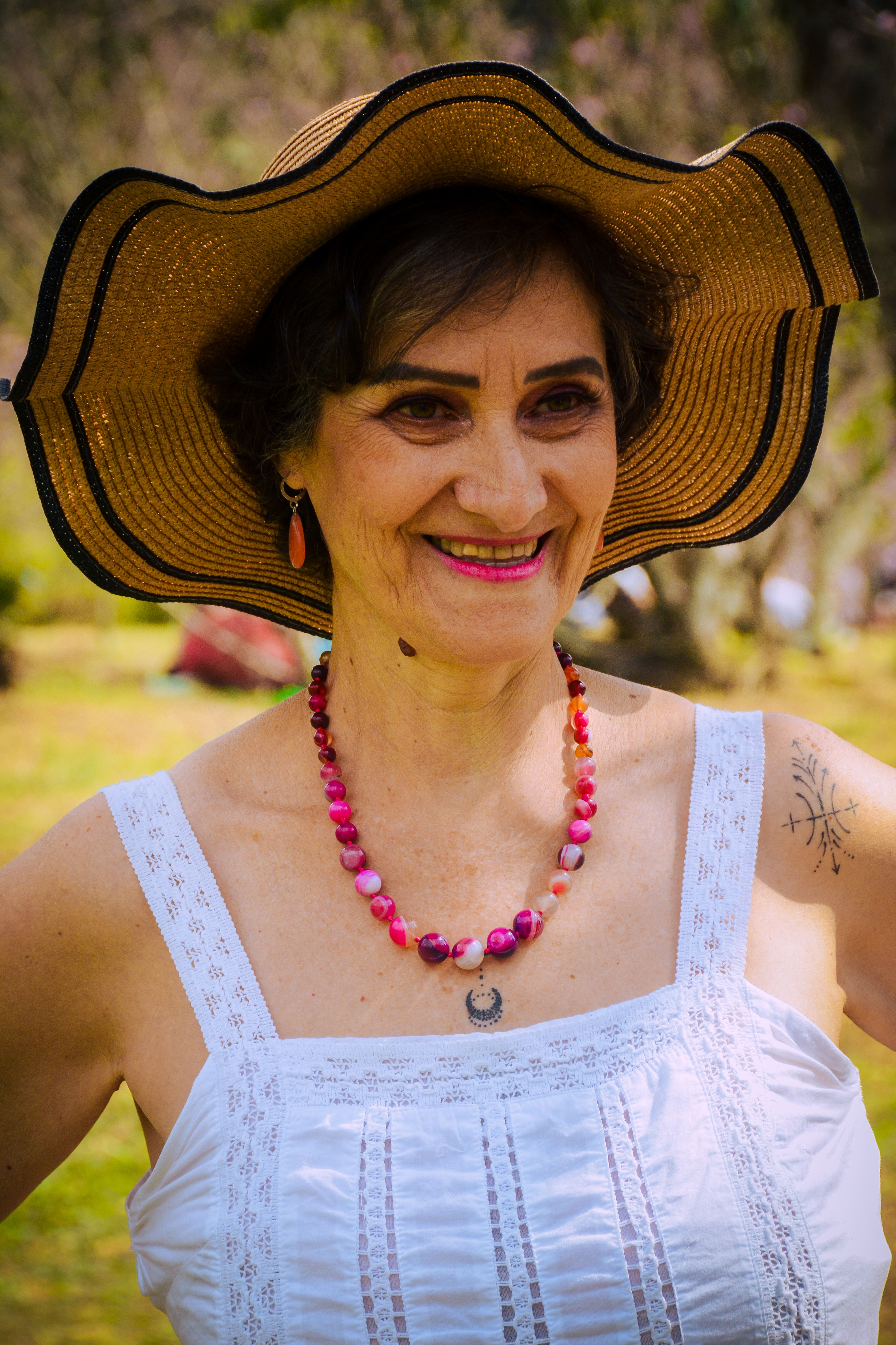 Joyful mature woman in a stylish sun hat smiling outdoors during summer.