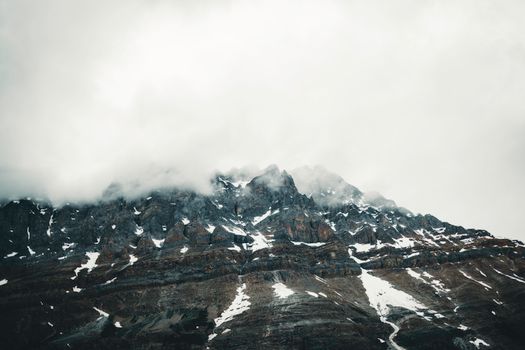 A striking view of a fog-covered rocky mountain peak in Banff, showcasing its snow-tipped edges.