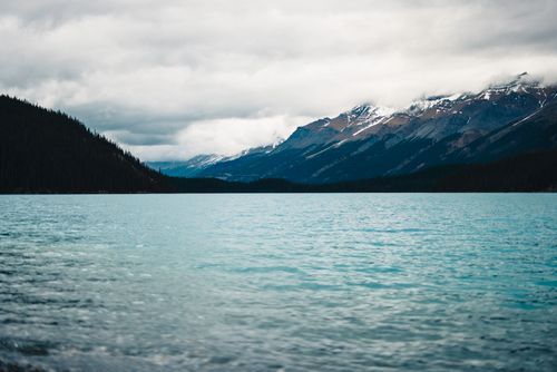 Free A serene view of a mountain lake in Banff National Park, Canada, with tranquil waters and snow-capped peaks. Stock Photo