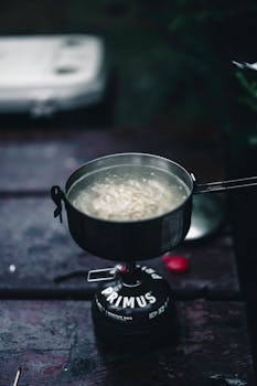 A pot of noodles cooking on a portable stove in Banff, Canada, featuring steam rising and dark ambiance.