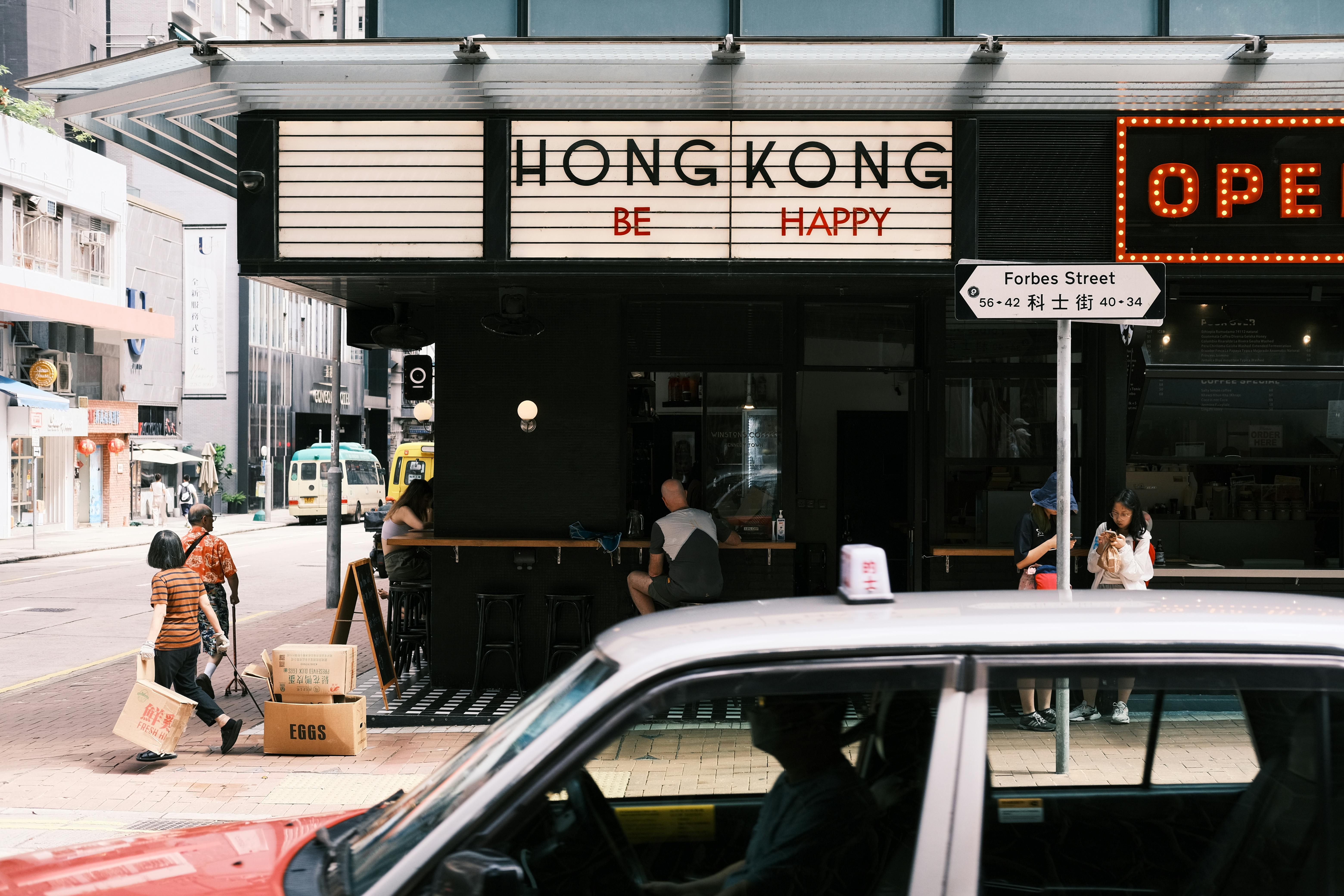 Dynamic street scene in Hong Kong featuring pedestrians and a café. Captures urban life.