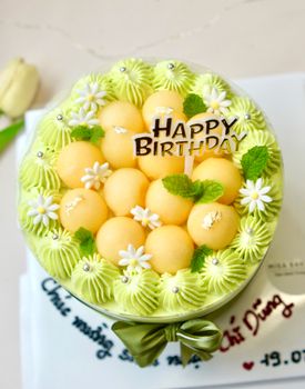 A beautifully decorated birthday cake with melon balls and floral accents, perfect for celebrations.