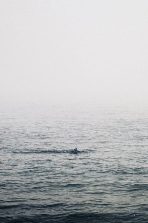 Free A lone swimmer moves through misty ocean waters, evoking solitude and adventure. Stock Photo