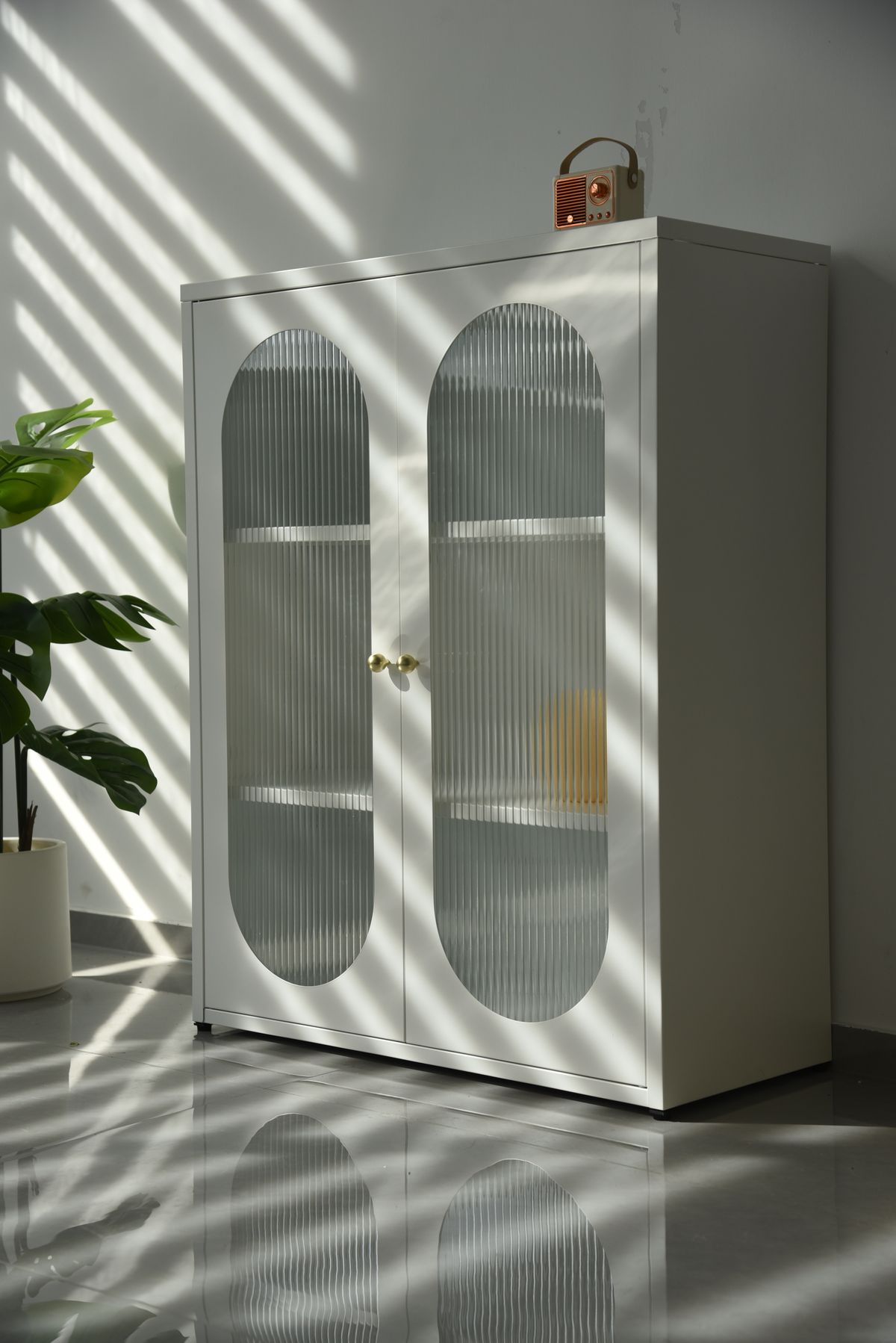 Elegant white cabinet with glass doors and a plant in a sunlit room