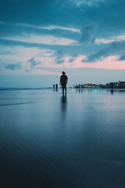 Free Silhouettes of people walking on a tranquil beach at sunset with a dramatic sky. Stock Photo