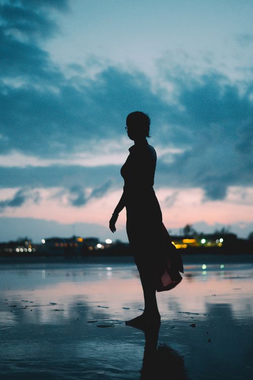 Free A serene silhouette of a woman standing on a beach at sunset, reflecting peace and solitude. Stock Photo