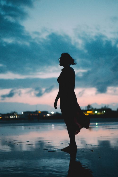 Free Silhouette of a woman standing on a serene beach during twilight, reflecting solitude and peace. Stock Photo