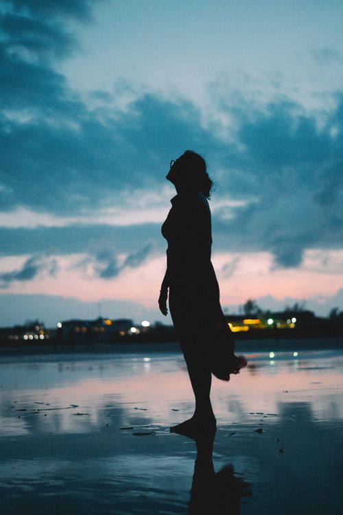 Free Silhouette of a woman reflecting in calm water at twilight, under a vibrant sky. Stock Photo