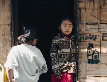 Two children standing at a rustic wooden doorway, bathed in sunlight.