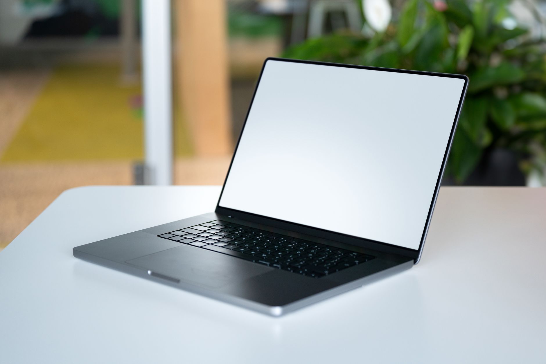 A modern laptop with blank screen placed on a white desk in an office environment, ideal for business presentations.