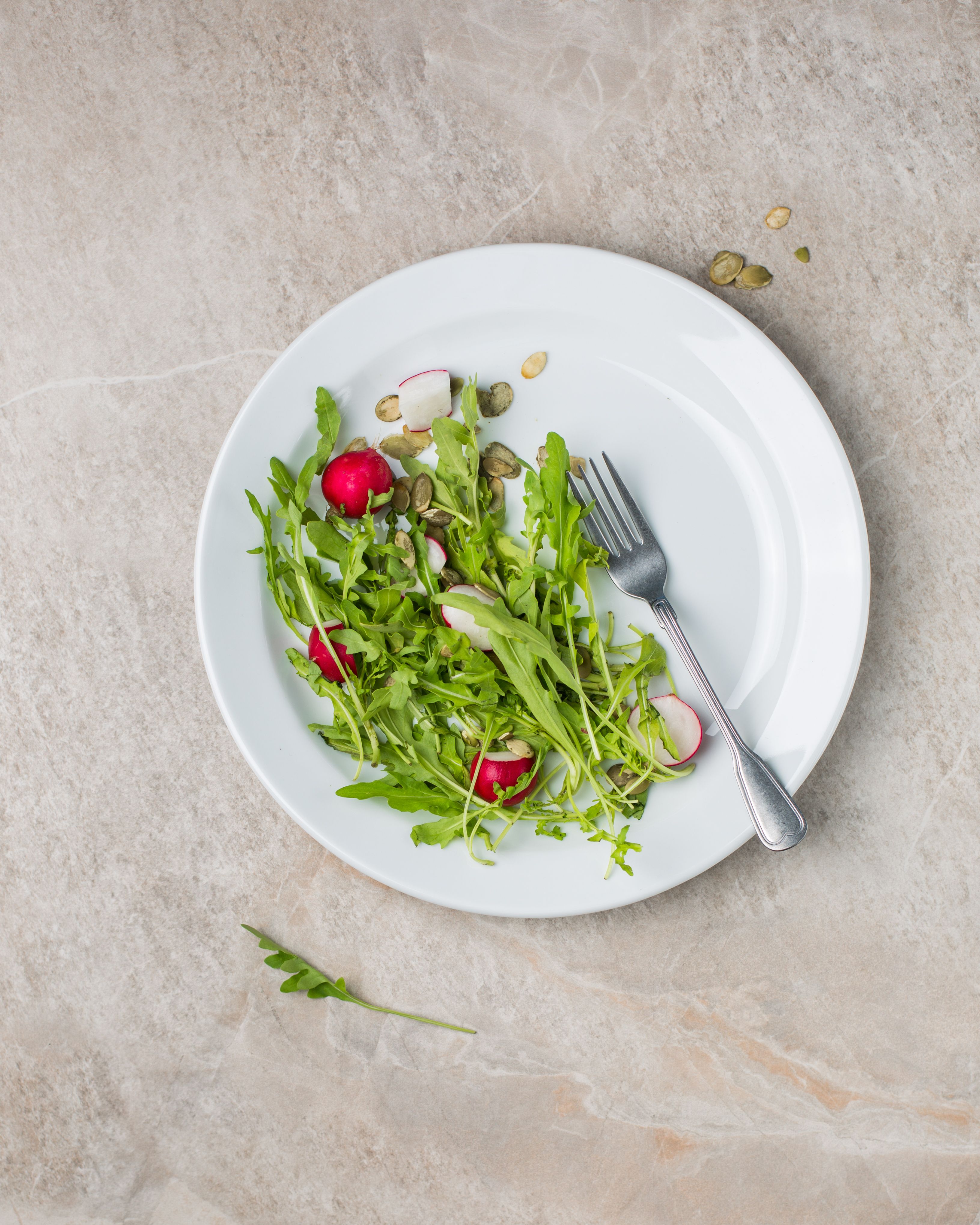 Healthy arugula and radish salad with seeds on white plate viewed from above.