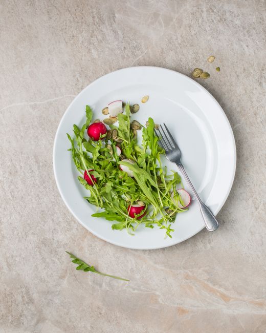 Healthy arugula and radish salad with seeds on white plate viewed from above.