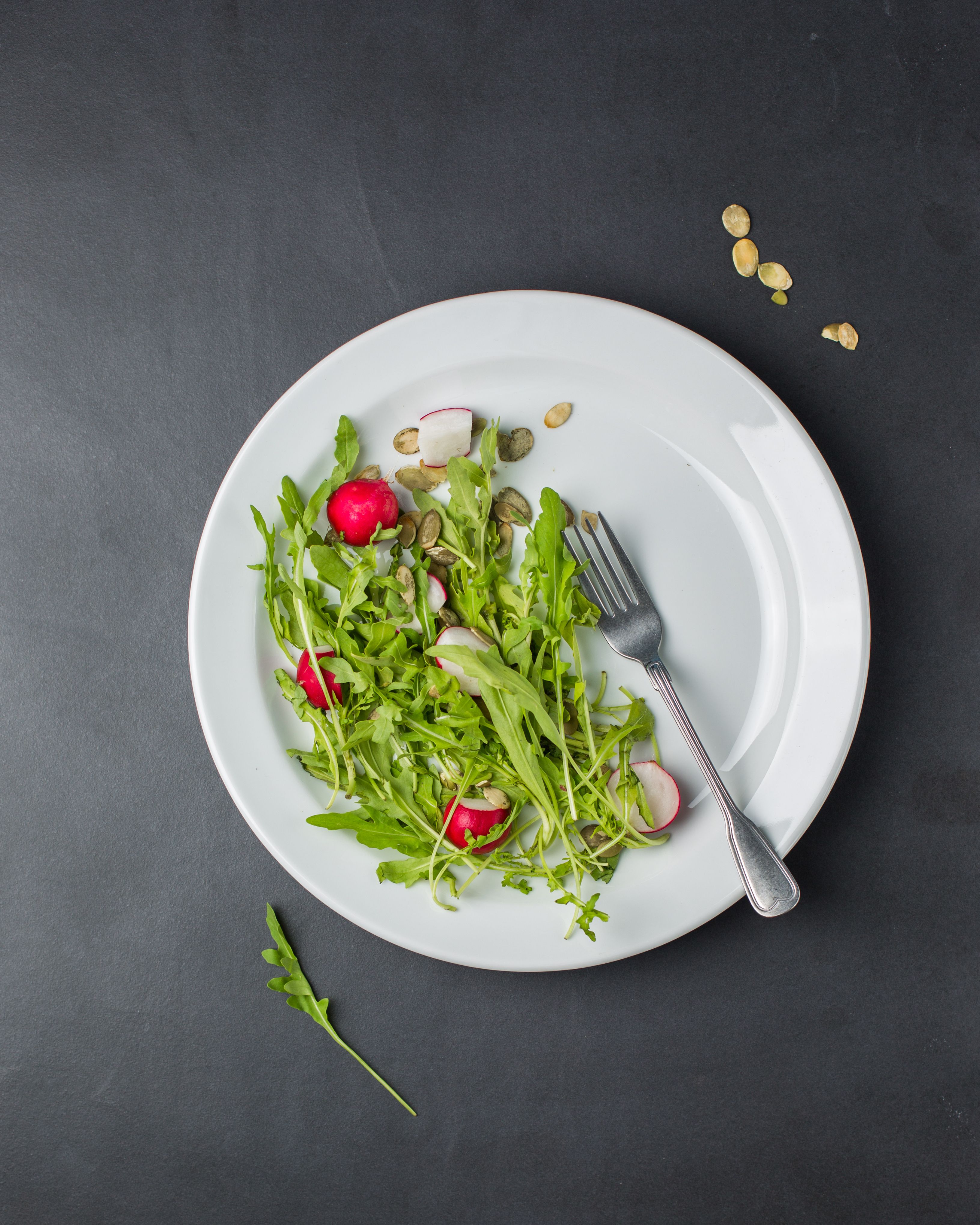 Fresh arugula and radish salad with seeds on a white plate, viewed from above.