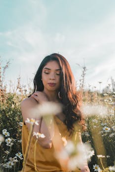 一名身穿黄色连衣裙的女子，在晴朗天空下的雏菊地里平静地摆着姿势