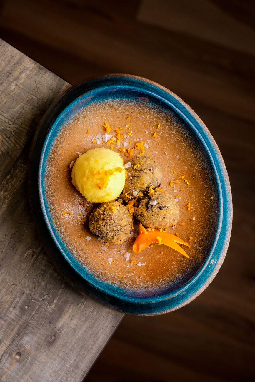 Close-up of a gourmet dessert with chocolate truffles and mango sorbet on a ceramic plate.