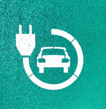 White electric vehicle charging symbol on textured green asphalt background. 27505892