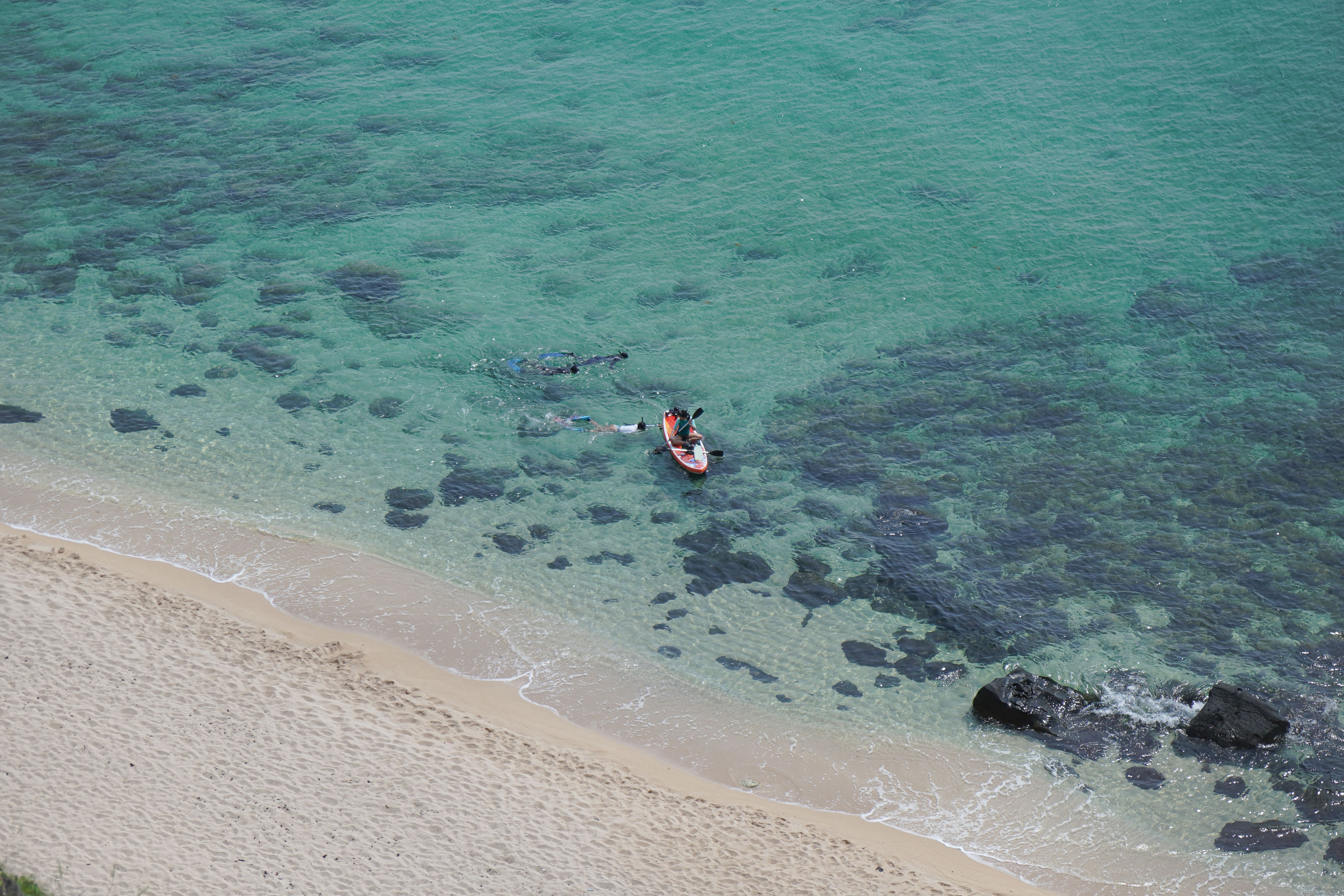 Aerial shot of snorkelers and kayak in turquoise waters near a tropical beach.