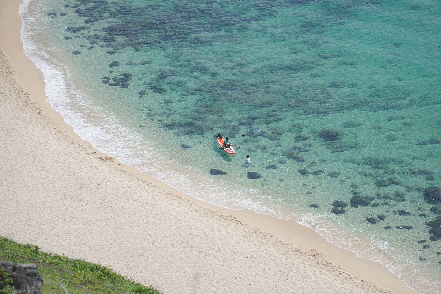 Scenic aerial view of Phan Thiết beach showcasing turquoise water and sandy shore with a canoe and people enjoying the s