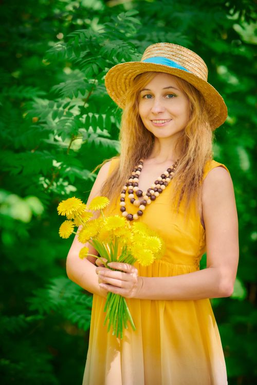 Free Woman in a summer dress and straw hat holding dandelions, depicting joy and nature's beauty. Stock Photo