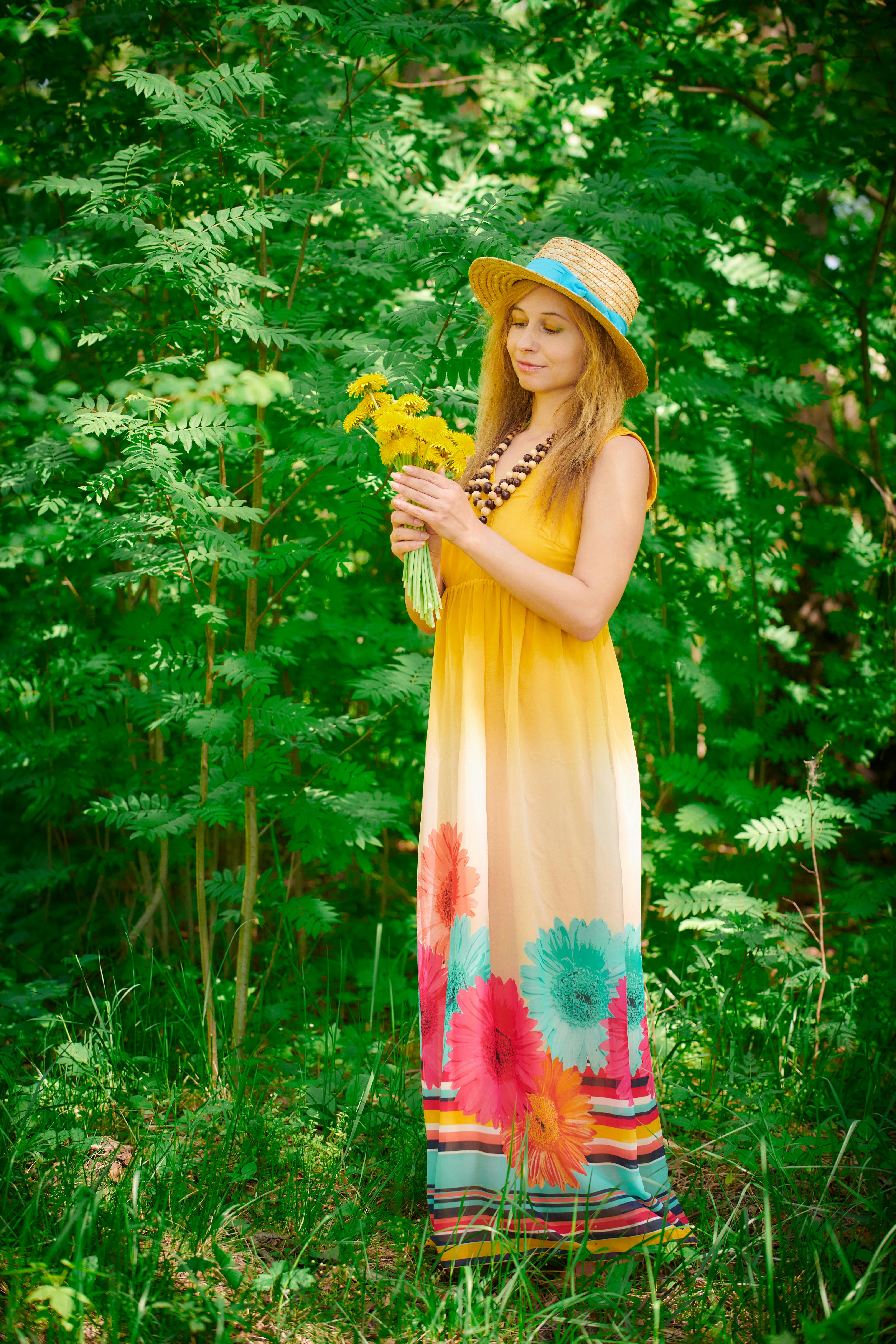 A woman in a colorful floral dress holds flowers, surrounded by lush greenery, exuding relaxation and joy.