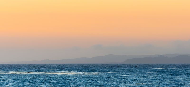 Sunset over open water with a distant headland — photo by Igor Passchier on Pexels