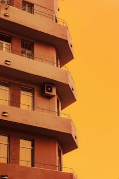 A modern apartment building with balconies silhouetted against a vibrant orange sky.