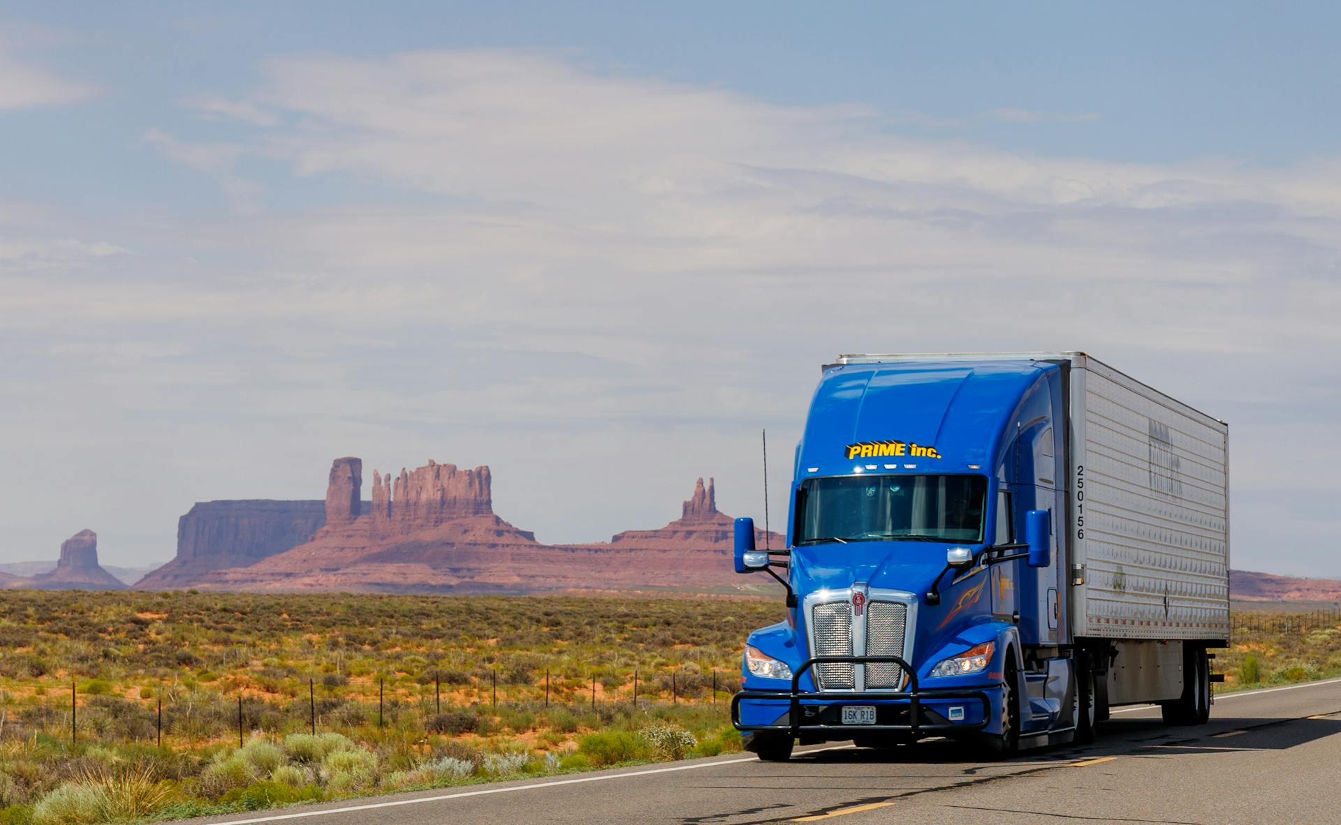 A blue semi truck driving down a desert road