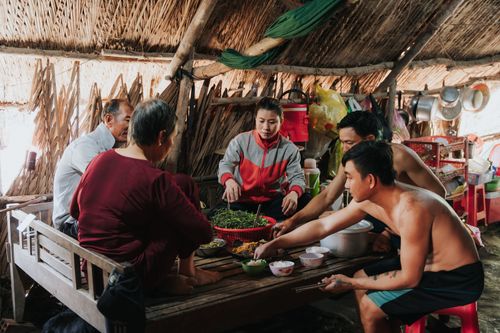 Free A rural family sits together indoors, enjoying a traditional meal with fresh vegetables. Stock Photo