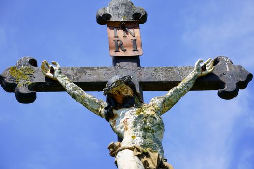 Free A weathered crucifix featuring Jesus stands against a bright blue sky, signifying faith and spirituality. Stock Photo