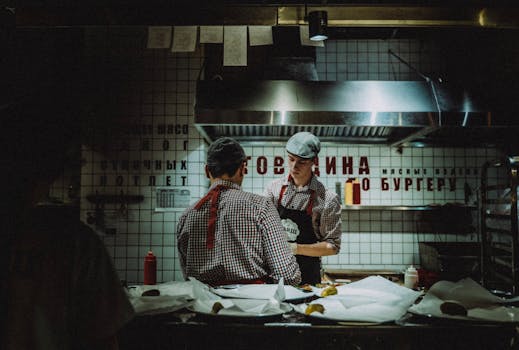 Chefs working in dimly lit kitchen, preparing food. Atmosphere is rustic and industrial.