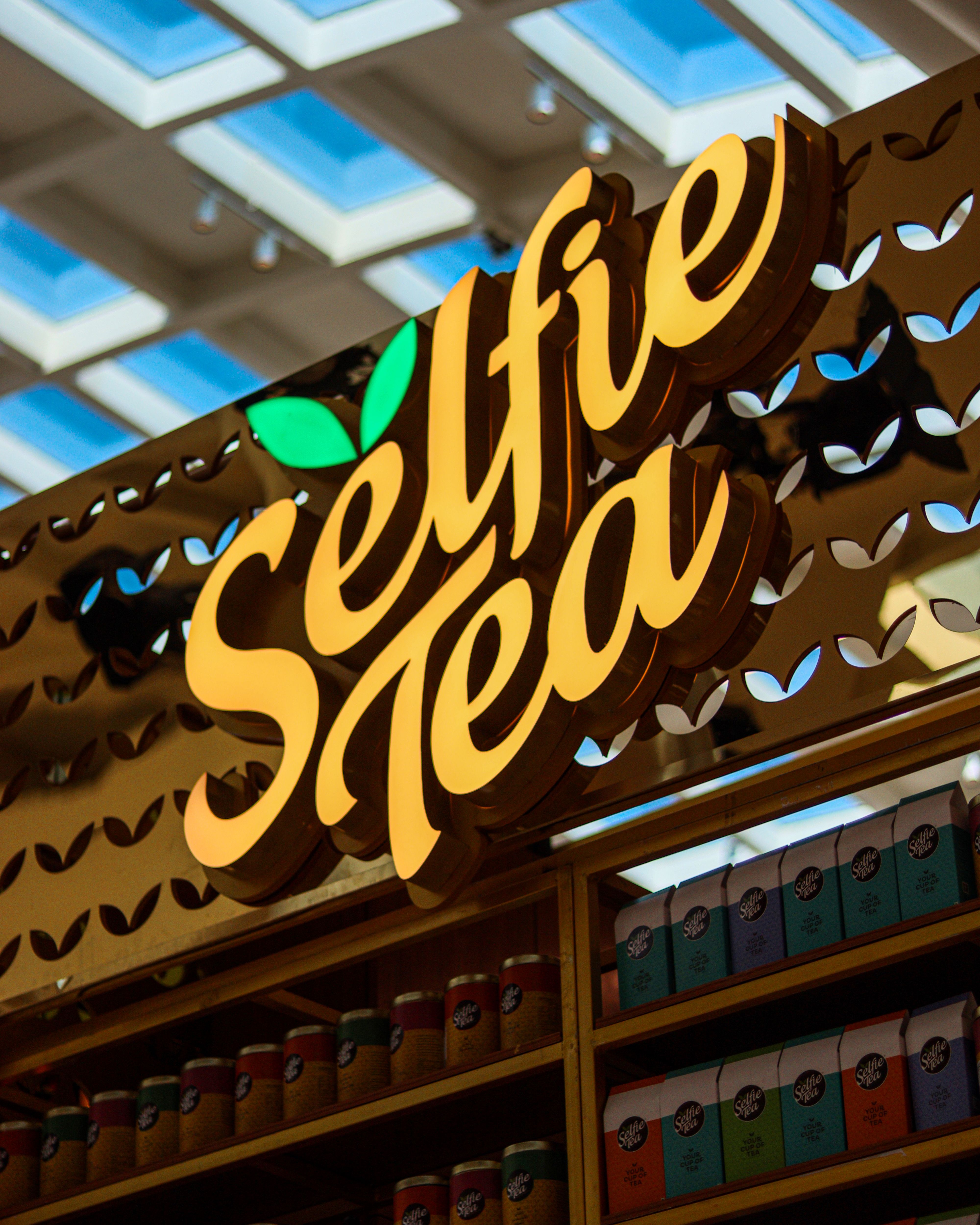 Bright Selfie Tea shop sign in an indoor shopping mall with colorful tea packaging displayed.