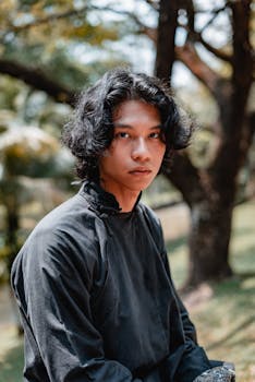 一名年轻人身着传统服装，在吉隆坡郁郁葱葱的公园里户外摆姿势