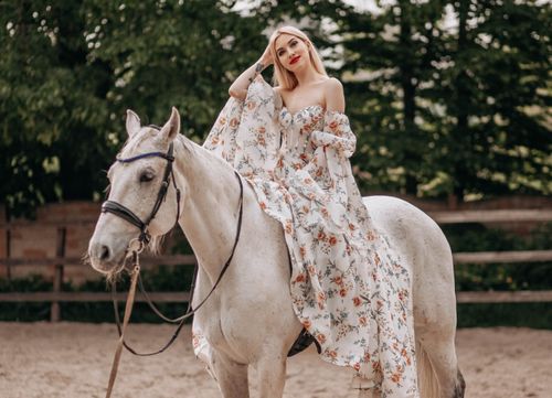 Free A beautiful woman in a floral dress elegantly seated on a white horse outdoors. Stock Photo